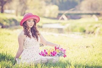 Young woman in pink hat sitting in field with flowers