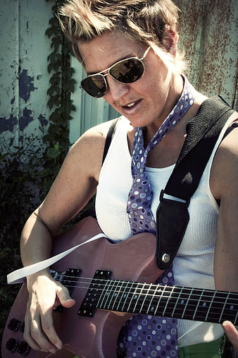 Woman playing pink electric guitar outdoors with sunglasses