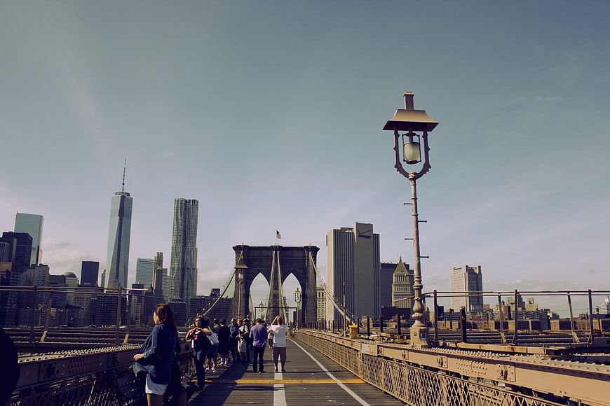 Pedestrians Walking On Brooklyn Bridge With Manhattan Skyline