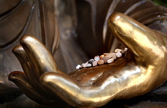 Close-up of golden Buddha statue hand holding small pebbles