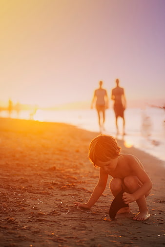 Toddler playing with sand on beach at sunset with parents
