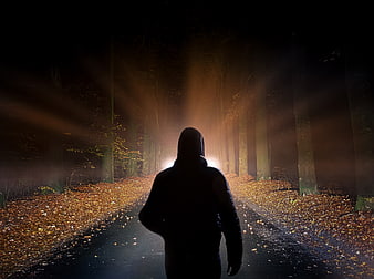 Silhouette of hooded figure walking on dark forest path at night