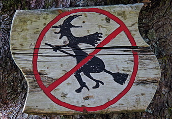 Hand-painted wooden sign with witch prohibition symbol on tree