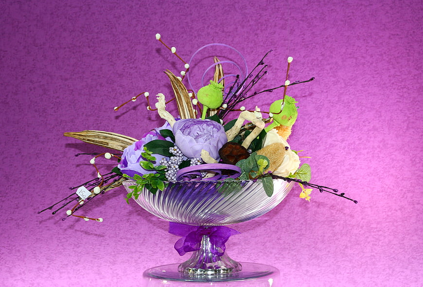 Purple floral arrangement in glass bowl on pink background