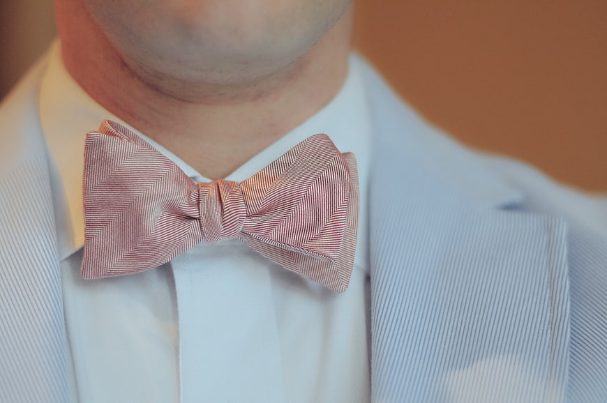 Close-up of man wearing pink herringbone bow tie and blue suit