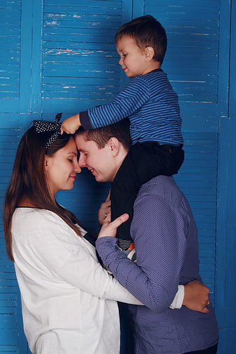 Family Portrait With Toddler On Shoulders Against Blue Wooden Background