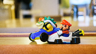 Mario and Bowser toy karts racing on wooden floor