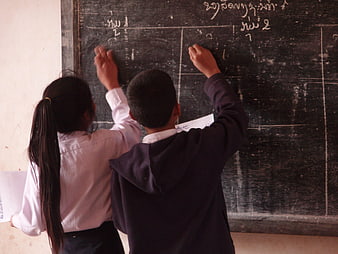 Two students writing on a chalkboard in a classroom