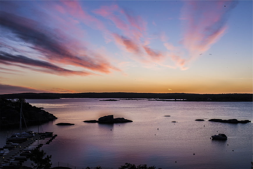 Dramatic Sunset Over Calm Harbor with Boats and Rocky Islands