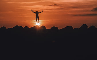 Silhouette of Man Jumping on Mountain Peak at Sunset