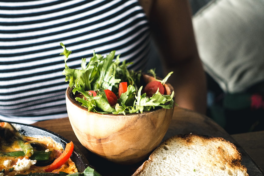 Fresh green salad in wooden bowl with toast and shakshuka