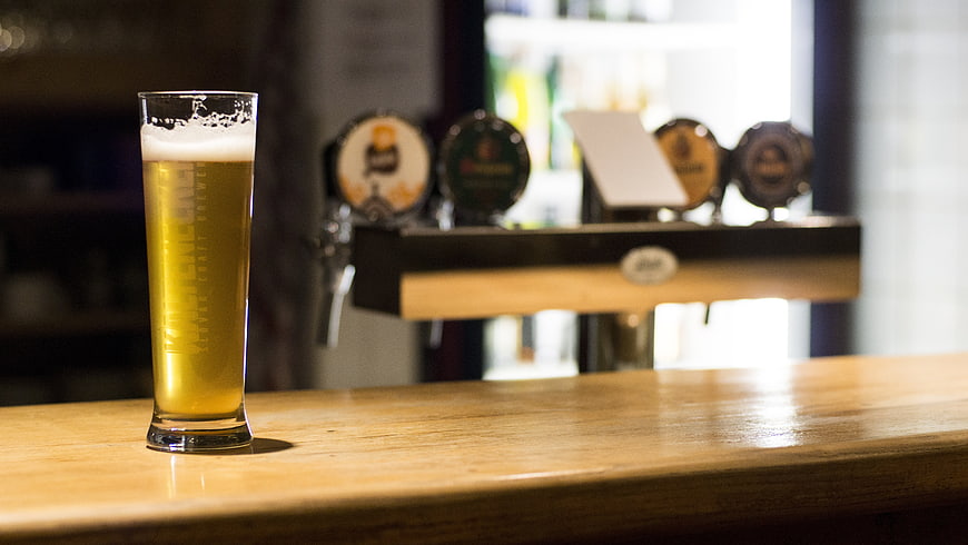 Glass of golden lager on wooden bar counter with blurred beer taps