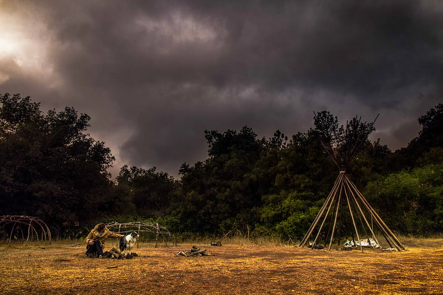 Woman and Dog in Camp with Teepee Under Stormy Sky