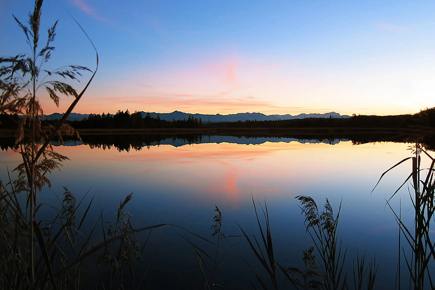 Serene Lake Sunset with Mountain Reflections and Reeds