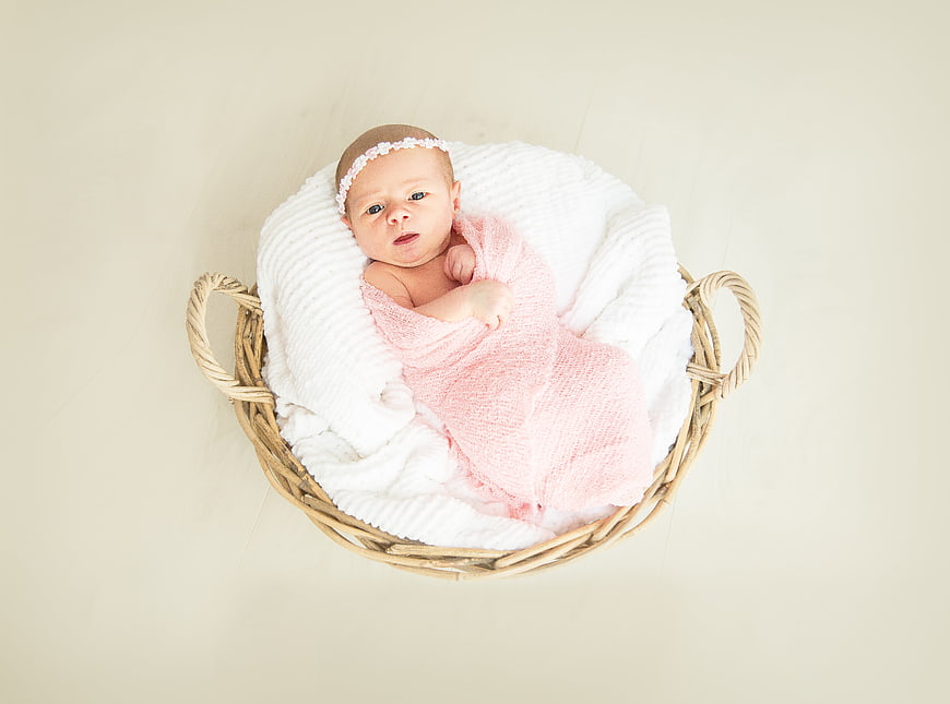 Newborn baby girl in wicker basket with pink wrap