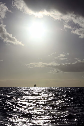 Silhouette of Sailboat on Ocean with Sunlight Reflection