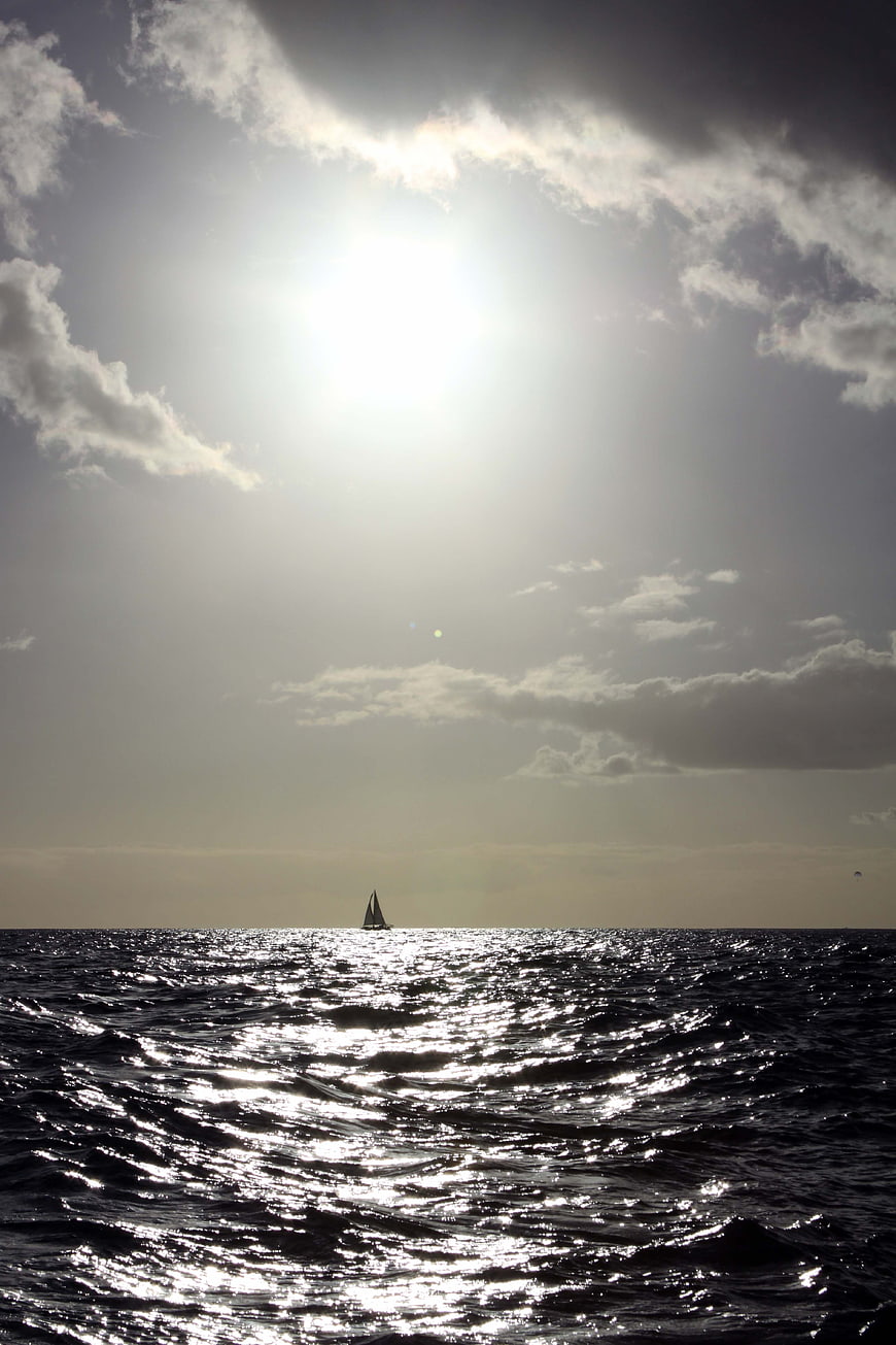 Silhouette of Sailboat on Ocean with Sunlight Reflection