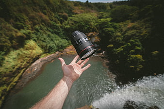 Hand tossing camera lens over waterfall canyon