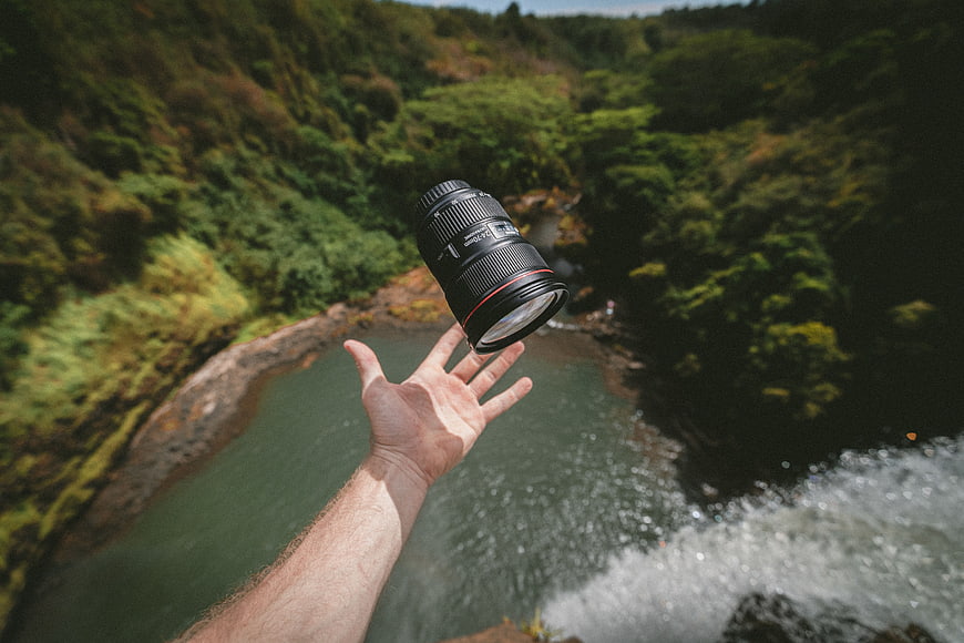 Hand tossing camera lens over waterfall canyon