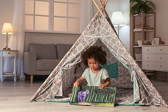 Cute child reading book inside play tent at home