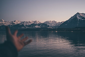 Blurred hand reaching toward snowy mountains at dusk