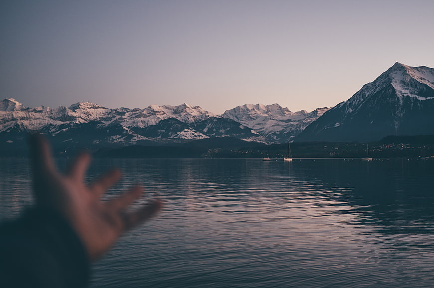 Blurred hand reaching toward snowy mountains at dusk