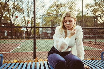 Melancholic blonde woman sitting on bench in autumn park