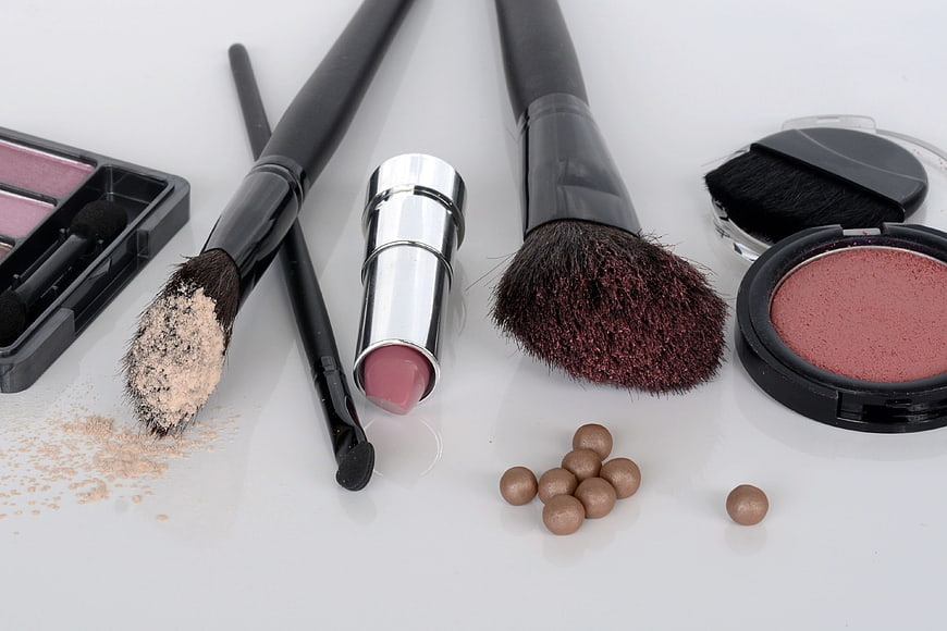 Flat lay of makeup brushes, lipstick, and blush on white background