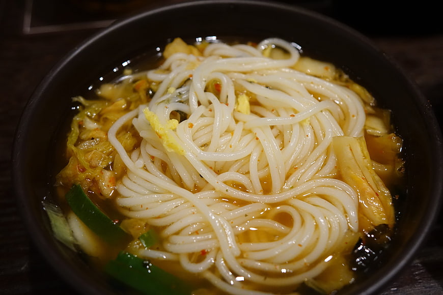 Close-up of white noodles in savory broth with vegetables in a dark bowl