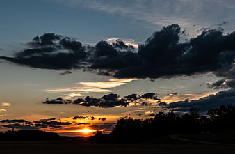 Dramatic sunset with dark clouds over silhouetted landscape