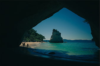 View of tropical beach and rock formation from inside a dark cave