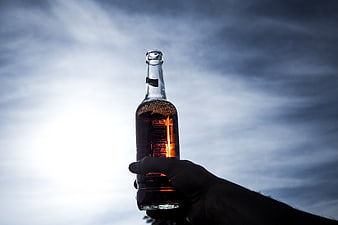 Hand holding amber beer bottle against dramatic cloudy sky