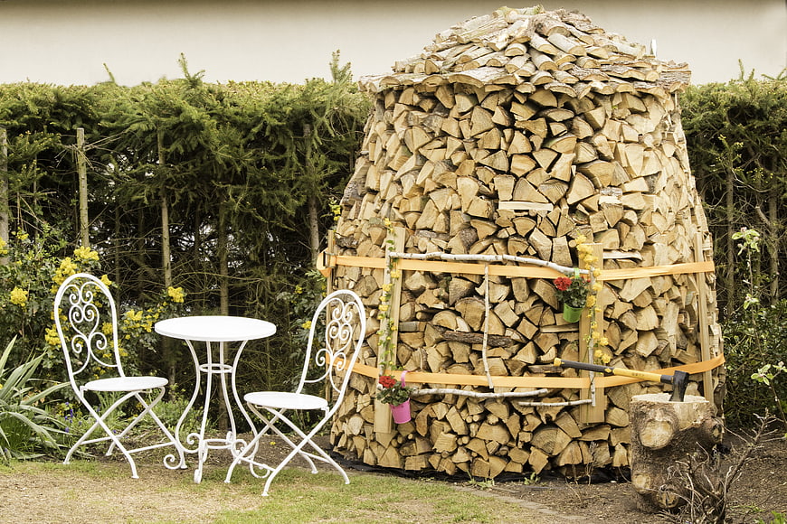 Rustic firewood stack with white garden furniture in backyard