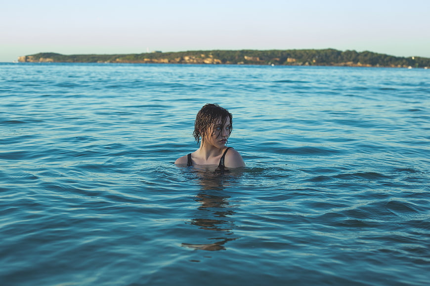 Woman Swimming in Blue Ocean Water with Coastal Background