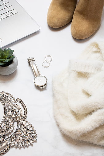 Flat lay of beige fashion accessories, laptop, and jewelry on white marble