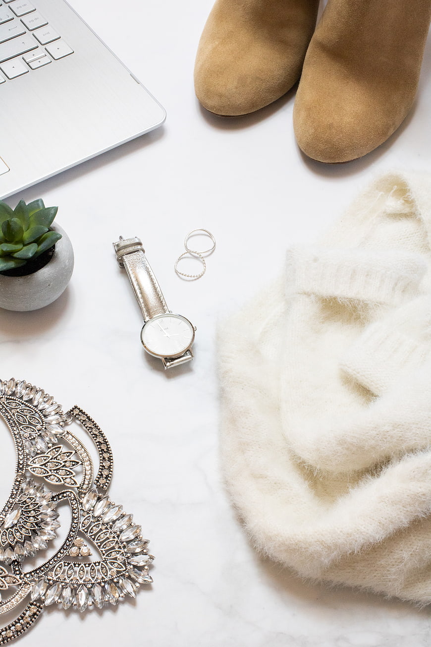 Flat lay of beige fashion accessories, laptop, and jewelry on white marble