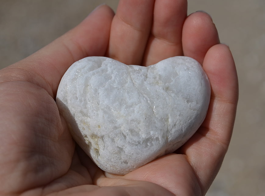 Hand holding white heart-shaped stone on sandy beach