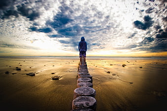 Man standing on stone path at beach sunset