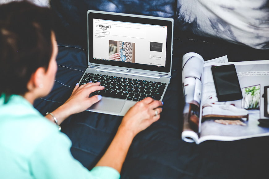 Woman browsing interior design website on laptop in bed