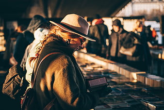 Woman in Fedora Reading Book at Outdoor Market Stall