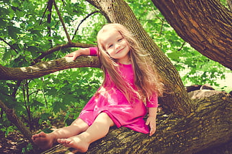 Happy little girl in pink dress sitting on tree branch