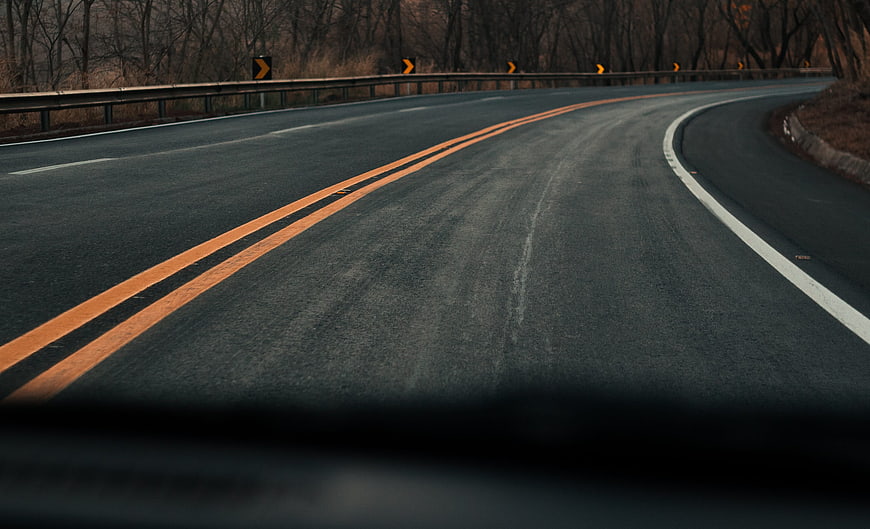 Curved asphalt road with yellow lines through bare forest
