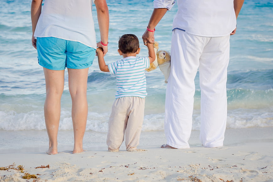 Family holding hands on white sandy beach looking at ocean