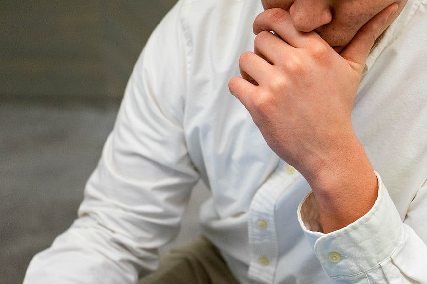 Close-up of man in white shirt holding chin in thought