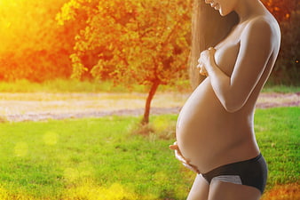 Pregnant Woman Holding Belly In Autumn Park