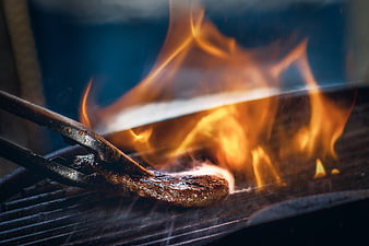 Close-up of steak grilling with intense flames and smoke