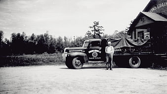 Vintage black and white photo of man standing by old truck