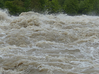 Powerful muddy floodwaters churning with white foam and splashes
