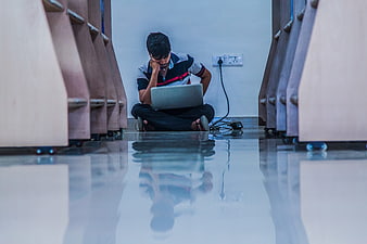 Young man studying on laptop sitting on floor between library shelves
