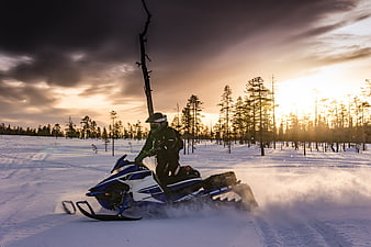 Snowmobile rider drifting in snowy forest at sunset